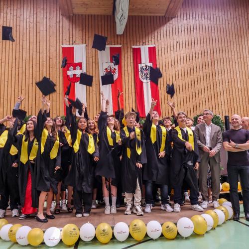 Die ist ein Gruppenbild der Klasse, während die AbsolventInnen die Hüte hochwerfen